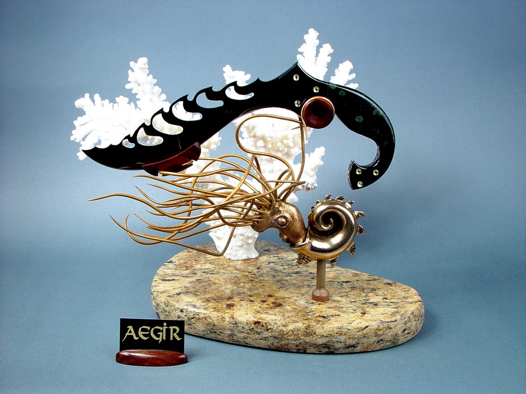 "Aegir" knife sculpture in mirror polished, hot blued O1 high carbon tungsten-vanadium alloy tool steel blade, blued steel bolsters, 14kt gold bezels, peridot gemstones, Nebula stone gemstone handle, stand of cast bronze, white Carribean coral, Venetian gold granite with garnets